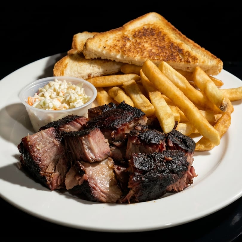 Plate of barbecued brisket, french fries, coleslaw, and toasted bread on a white plate.